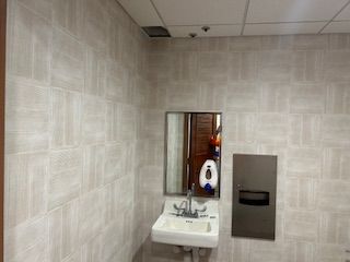 A modern restroom sink with a mirror and paper towel dispenser mounted on a wall covered in light, patterned tile.