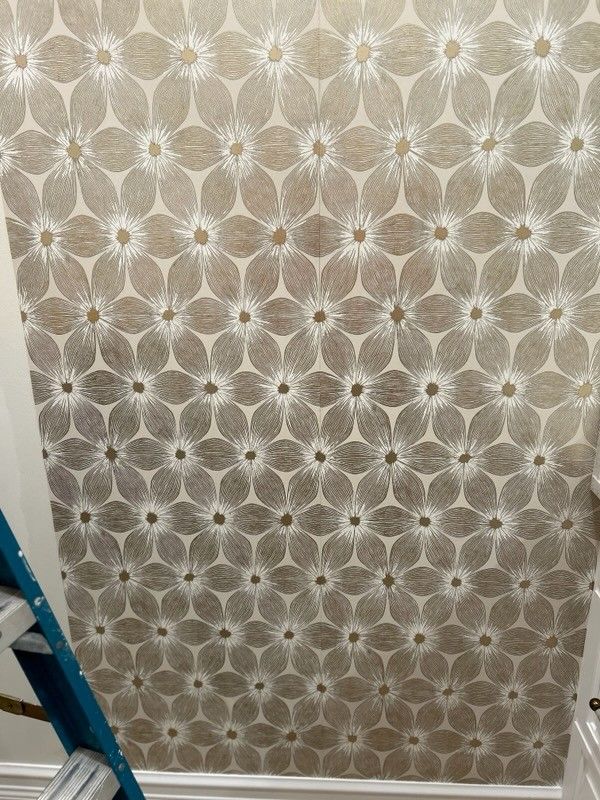 Wallpaper featuring a repeating floral geometric pattern in shades of beige, tan, and white.
