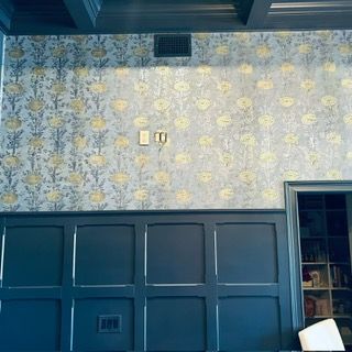 A room with dark blue wainscoting and upper walls covered in a floral wallpaper with yellow flowers on a blue background.