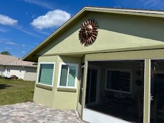 A light green house exterior with a decorative metal sun wall ornament, windows, and a screened-in patio.