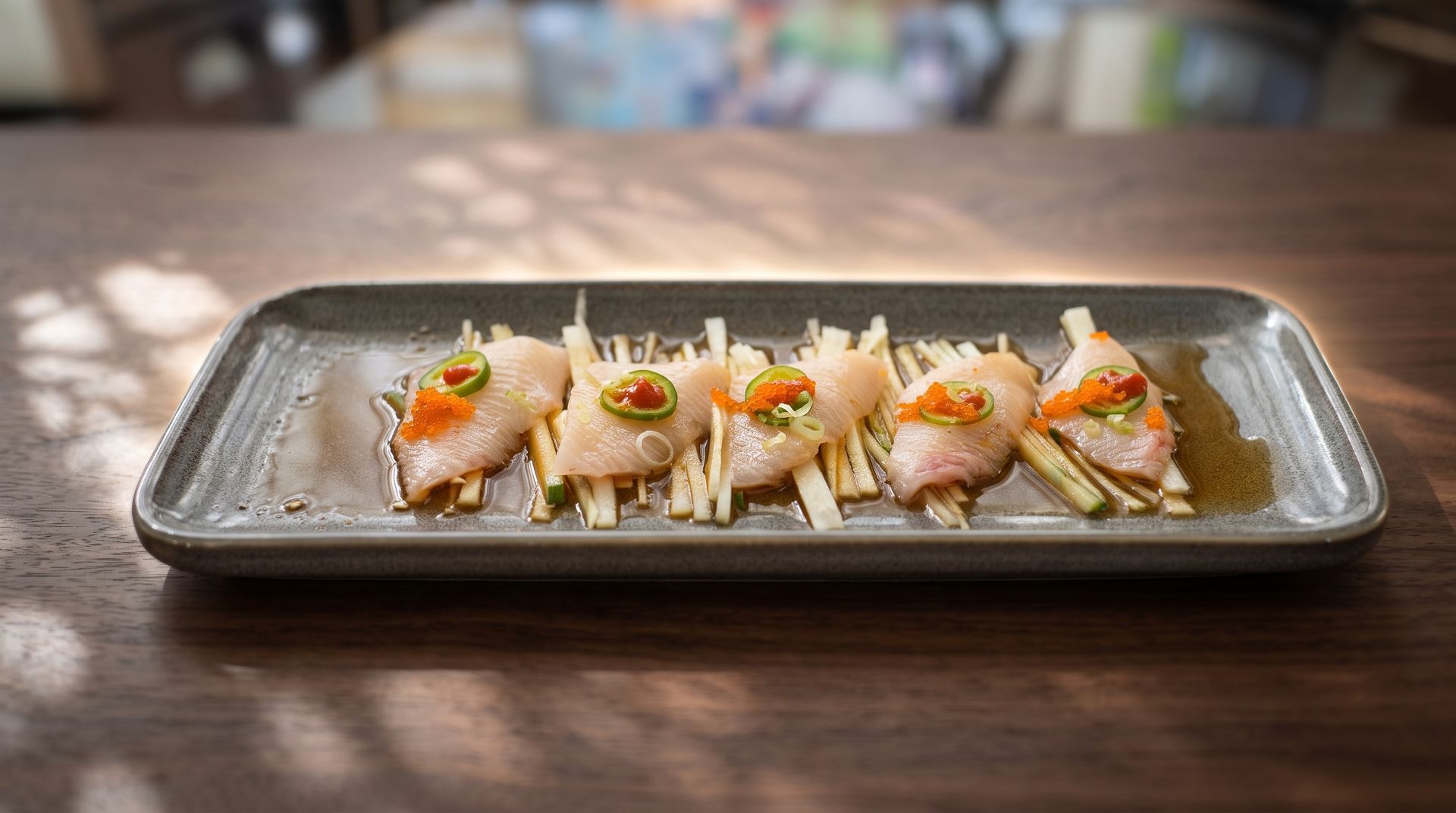 Five gourmet sushi pieces on a rectangular tray on a wooden table, topped with sauce and garnishes