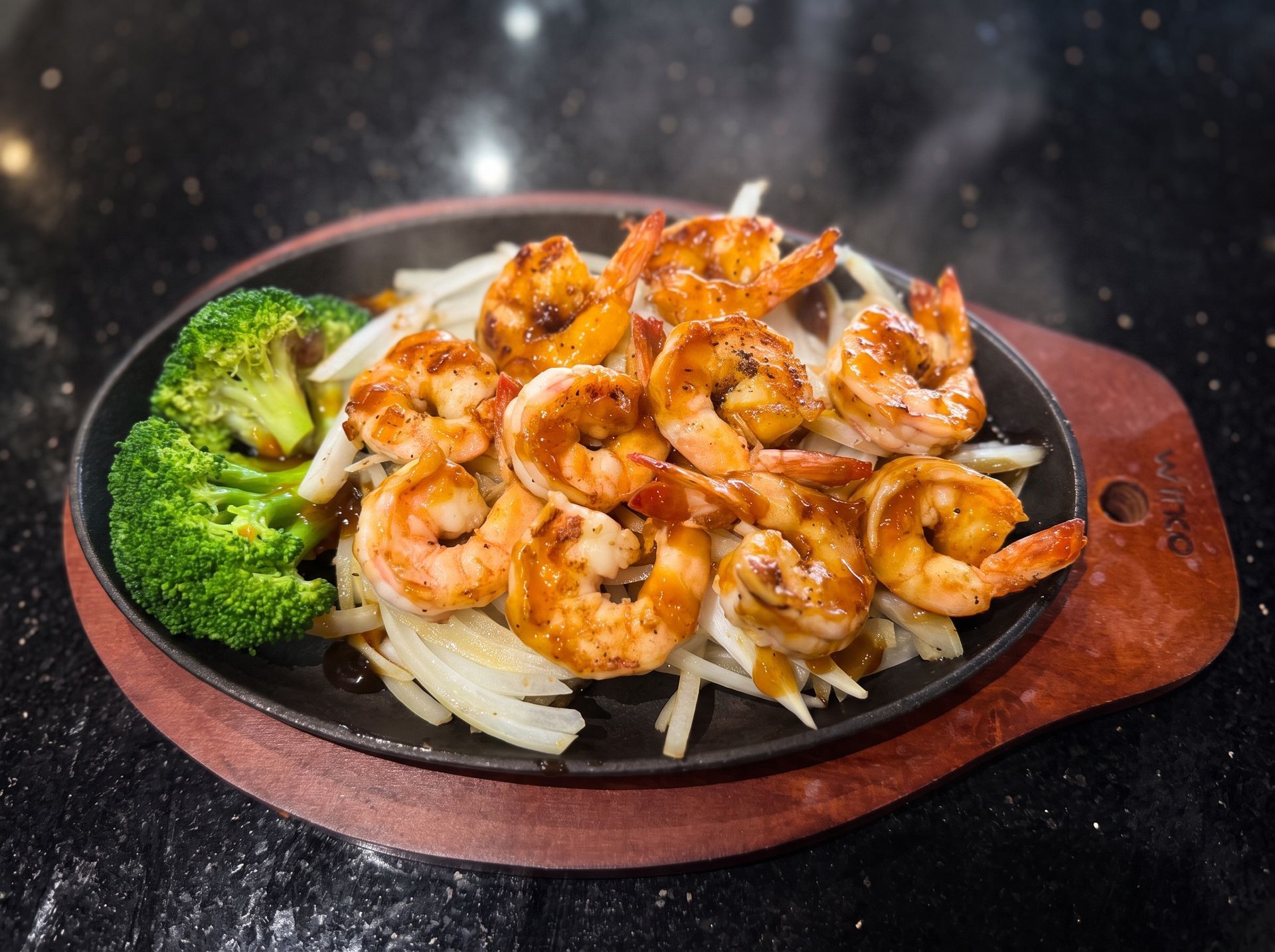 Grilled shrimp on a black plate with broccoli and onions on a wooden board