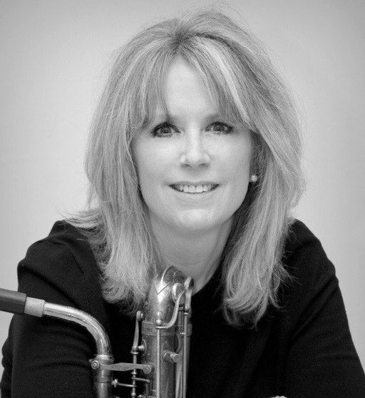 A person with shoulder-length hair poses in a black top, holding a saxophone. Black and white, portrait-style.