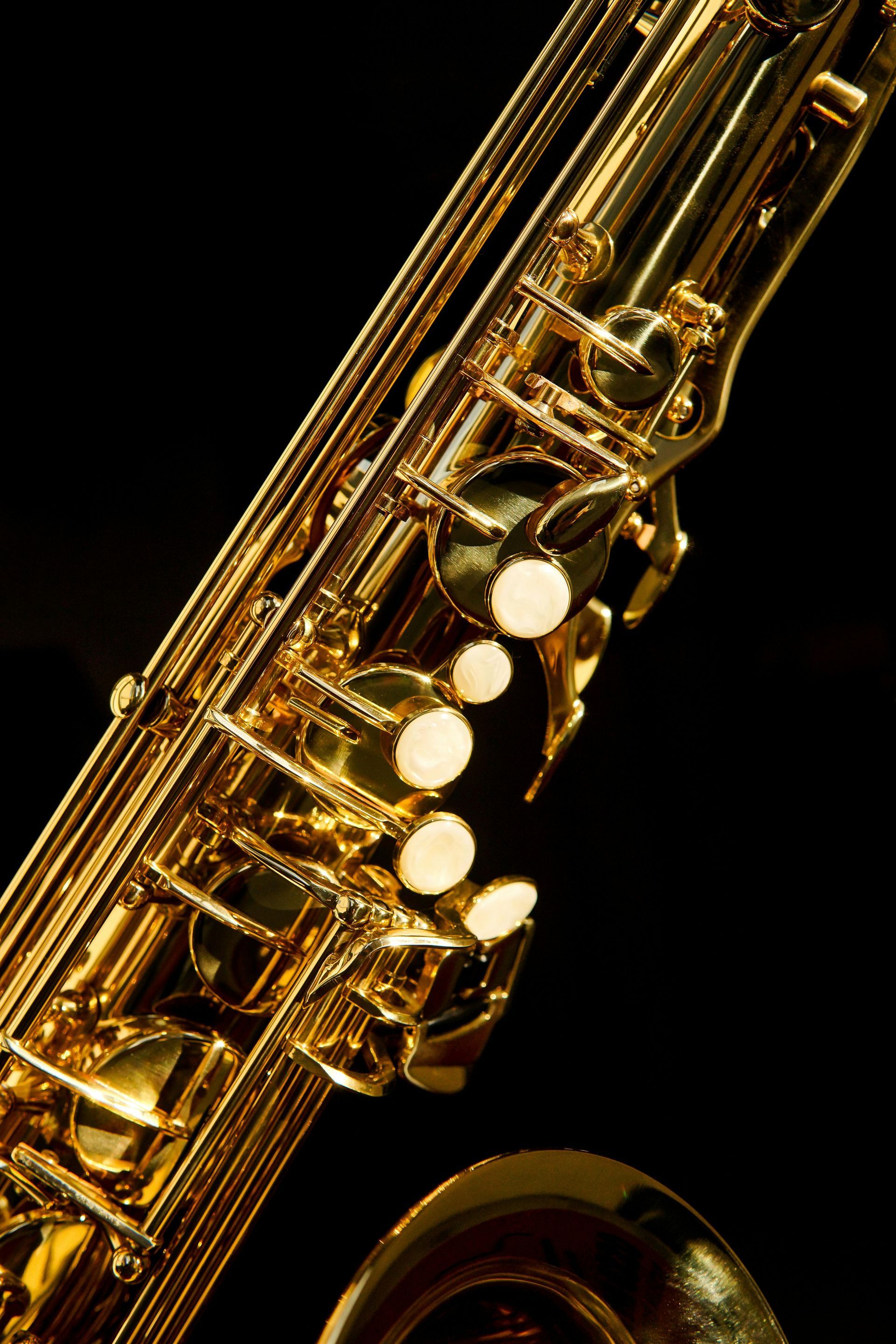 Close-up of a gold saxophone with white keys against a black background
