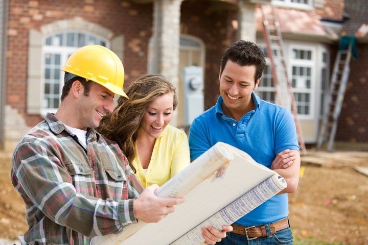 Construction worker showing house plans to a smiling couple in front of a new home.