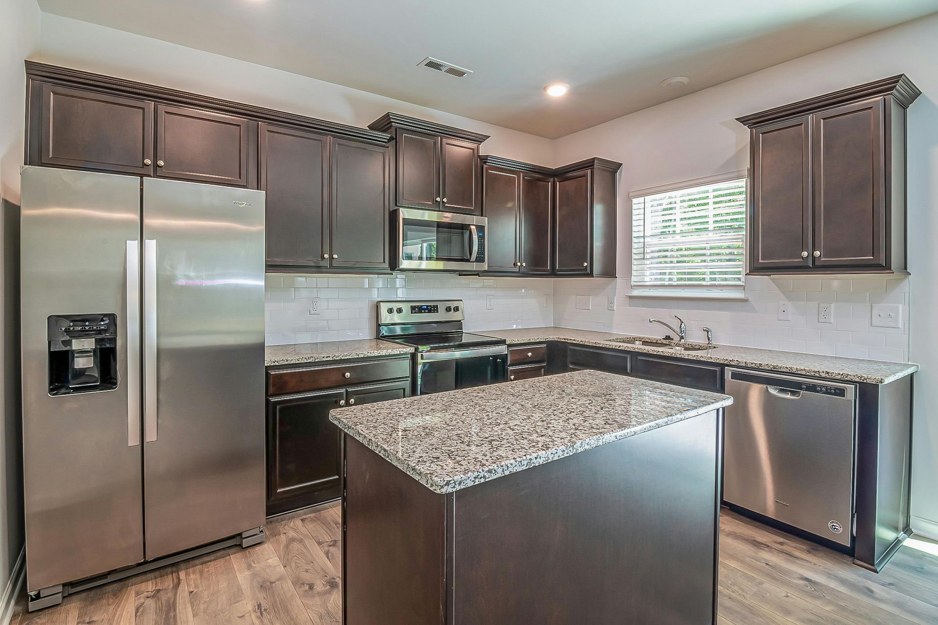 Modern kitchen with granite stone finishes and kitchen island. Large two-door fridge at the back.