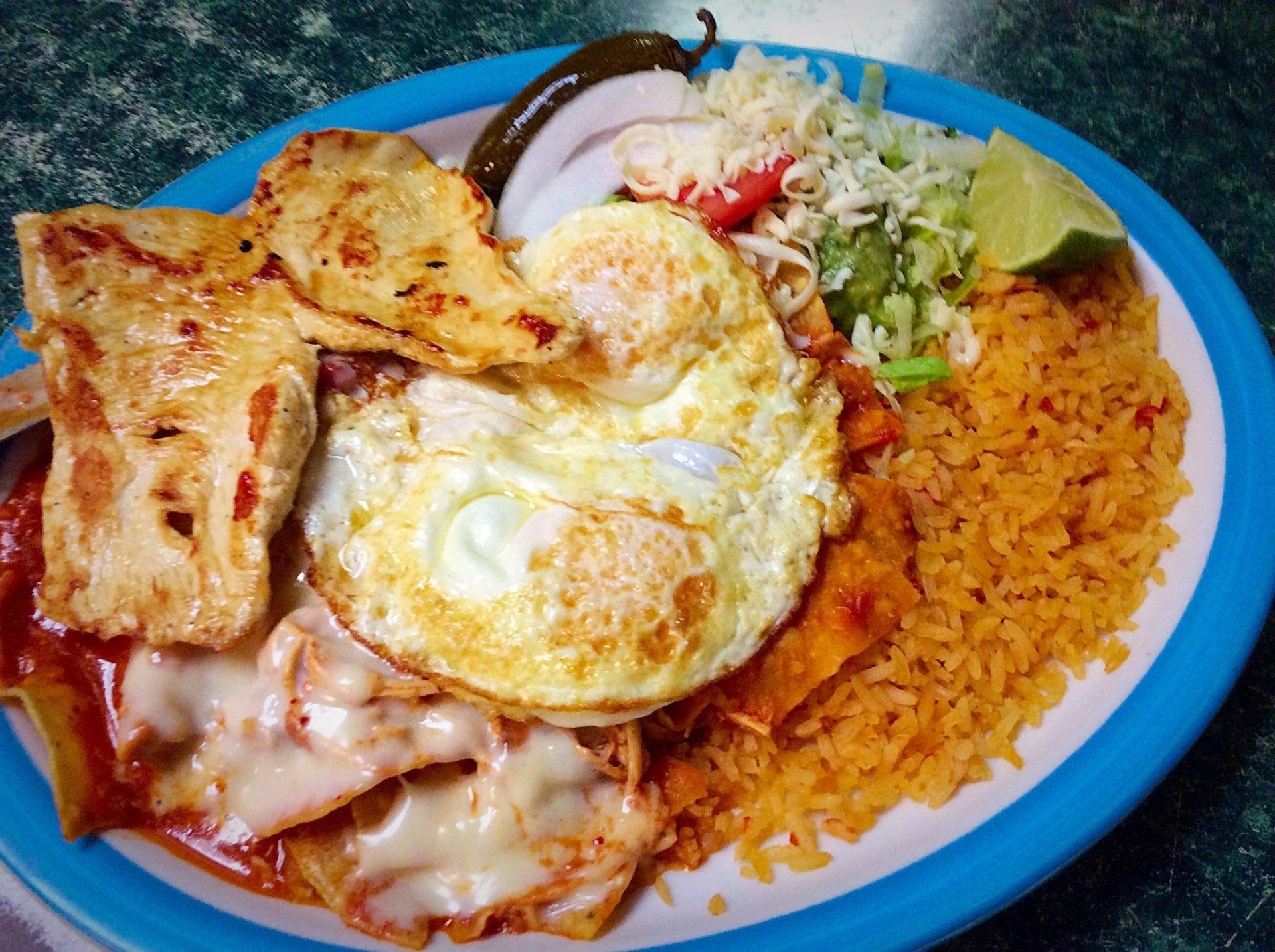 Plate of Mexican food: eggs, enchiladas, chicken, rice, salad, jalapeño, lime, and onion.