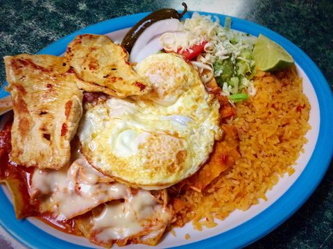 Plate of Mexican food: eggs, enchiladas, chicken, rice, salad, jalapeño, lime, and onion.