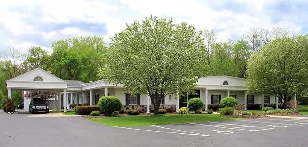 A single-story building with a carport, surrounded by trees and a paved parking area.
