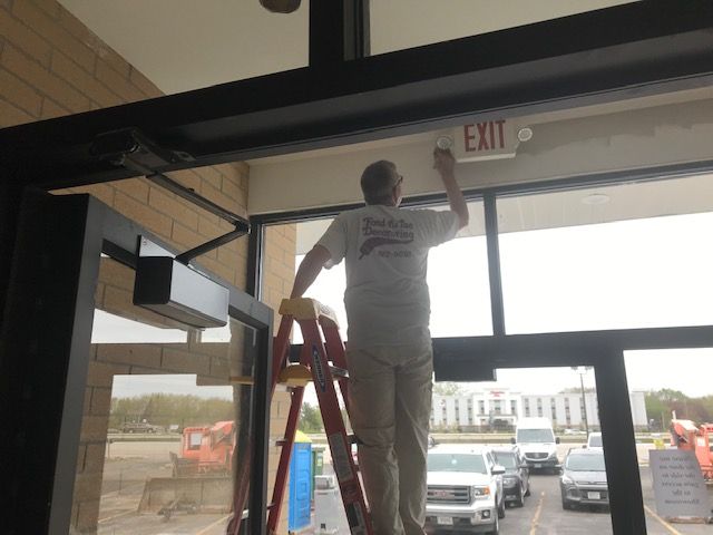 A man on a ladder paints an exit sign