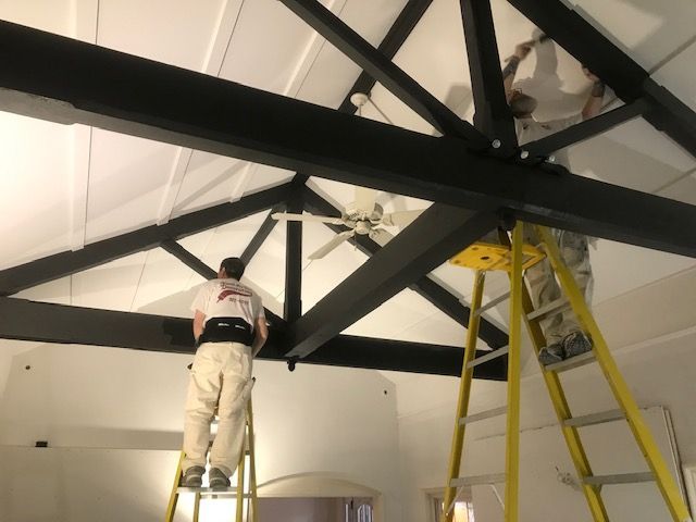 A man on a ladder painting a ceiling fan