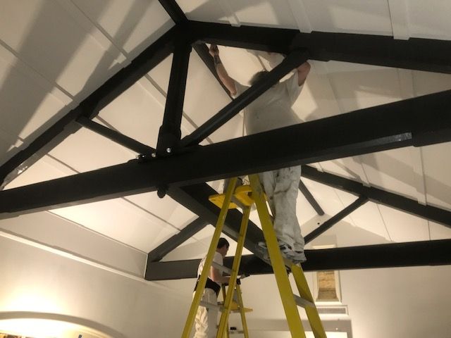 A man is standing on a ladder looking up at the ceiling