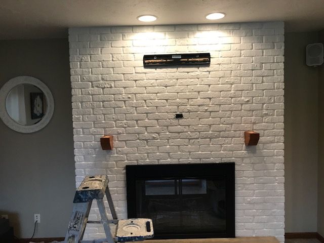 A living room with a white brick fireplace and a ladder.