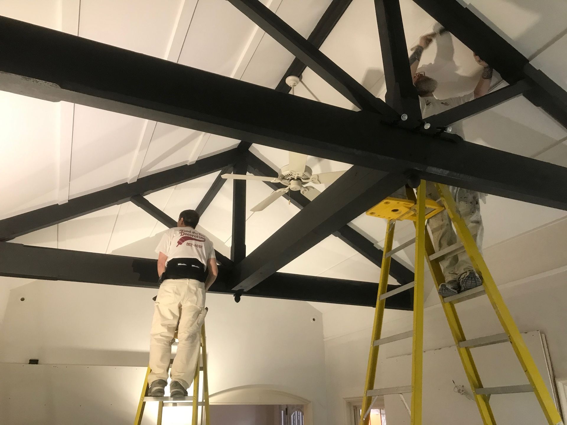 A man standing on a ladder painting a ceiling fan