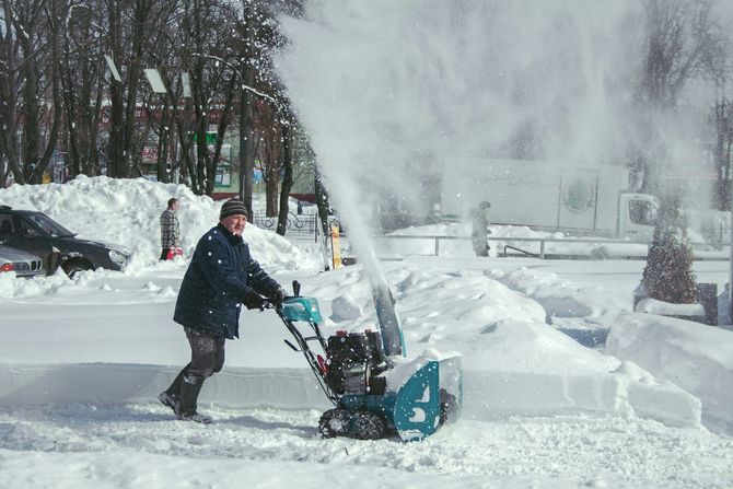 Person using a snow blower to clear a snowy driveway amid blowing snow