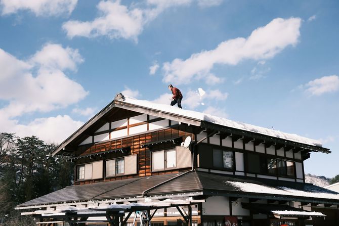 Two-story house with a worker on the roof under a blue sky