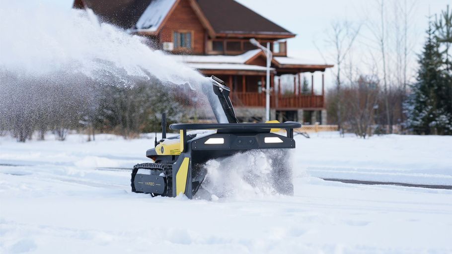 Yellow snowblower clearing deep snow in front of a house on a snowy driveway