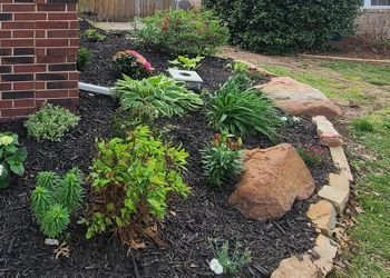 A garden with lots of plants and rocks in front of a brick building.