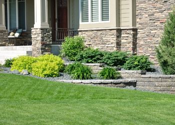 A house with a lush green lawn and a stone wall in front of it.