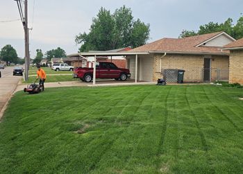 A man is using a lawn mower to cut the grass in front of a house.