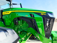 Green John Deere tractor cab and hood with yellow accents, shown close-up outdoors on a sunny day.