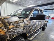 Pickup truck with camouflage vinyl wrap in an indoor garage or workshop.