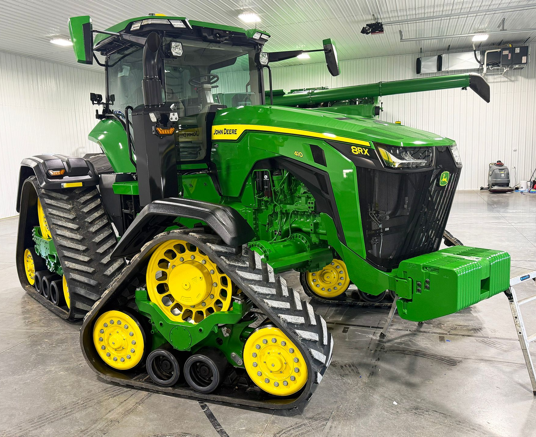 Green John Deere tractor with rubber tracks in a showroom, viewed from the side