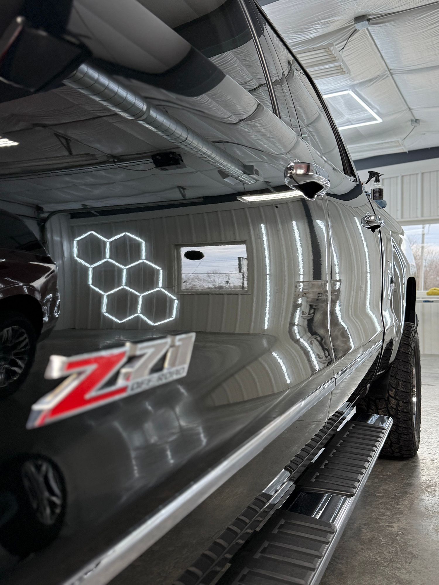 Glossy black Chevrolet Silverado with Z71 decal in a garage, reflecting hexagonal ceiling lights