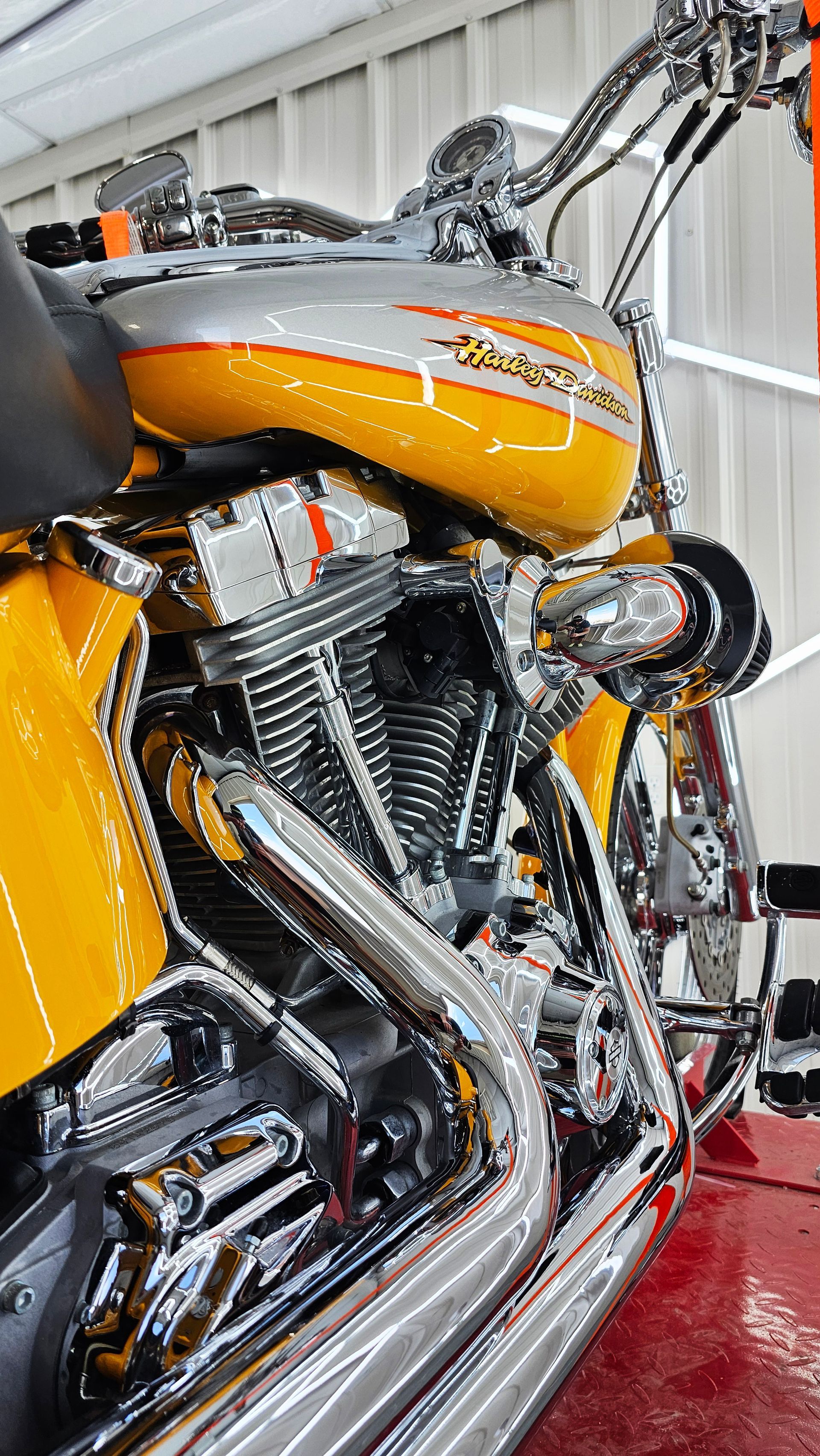 Close-up of a chrome motorcycle with an orange fuel tank and shiny engine in a showroom or garage.