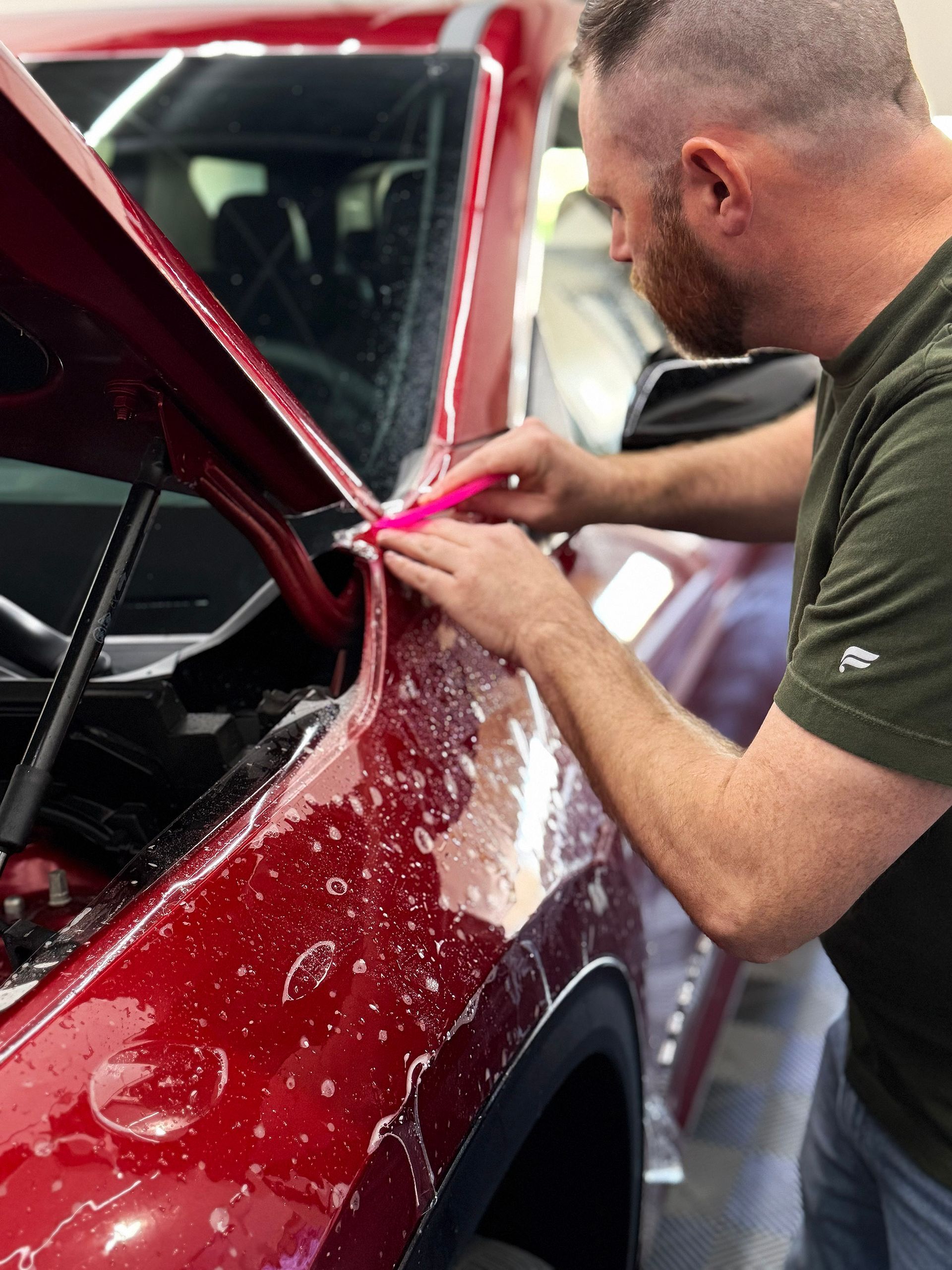 Man applying clear film to a red fender in a workshop