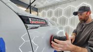 A person uses a  polisher to buff the painted surface of a vehicle.
