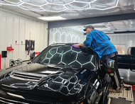 A technician stands on a step stool, buffing the roof of a black truck in a shop.