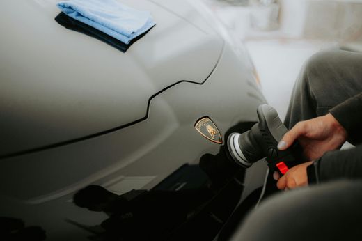 A close-up of a person using a power buffer to carefully polish around the front emblem on the hood of a car.