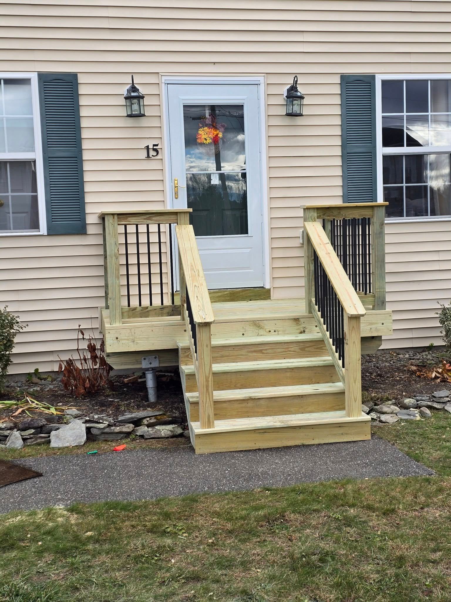 Front steps and ramp leading to a beige house’s white front door with autumn wreath.