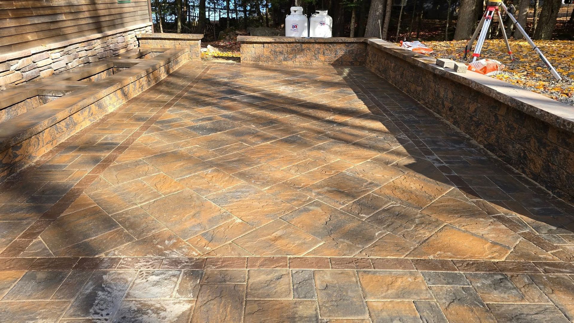 A stone-paved empty courtyard with steps, sunlit shadows, and trees in the background.