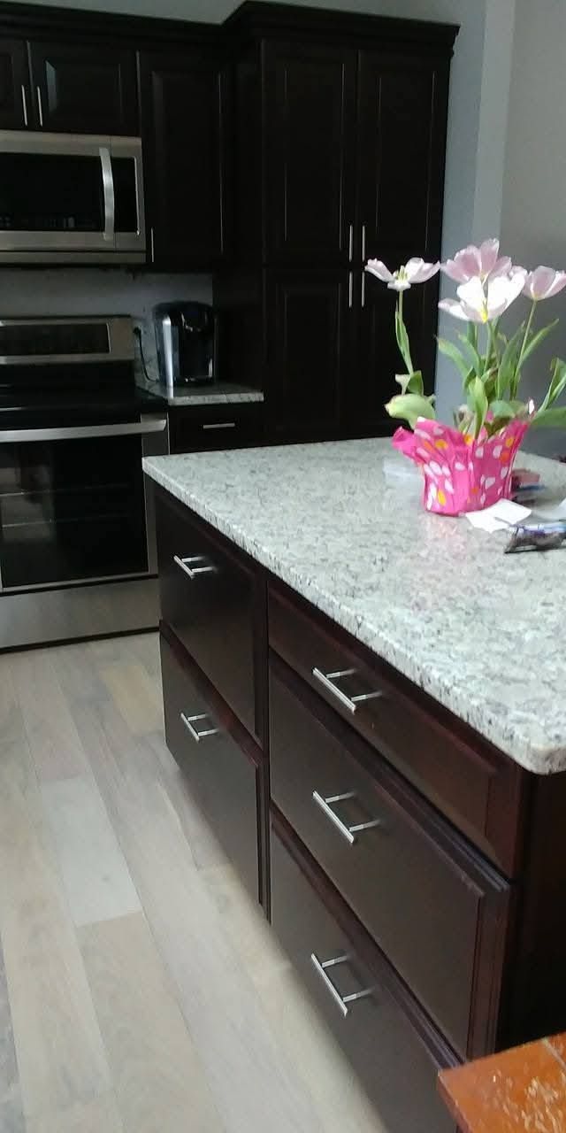 Modern kitchen with dark cabinets, light granite island, and a pink potted flower arrangement on the counter