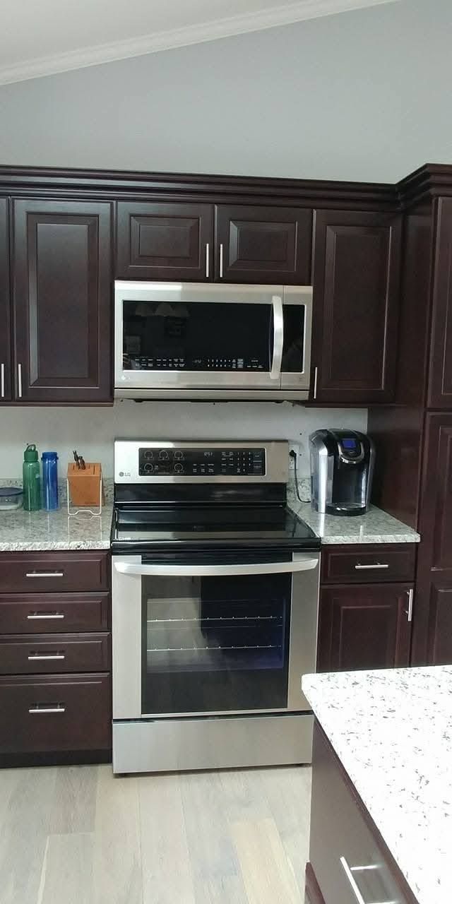 Modern kitchen with dark wood cabinets, stainless steel appliances, and a white countertop.