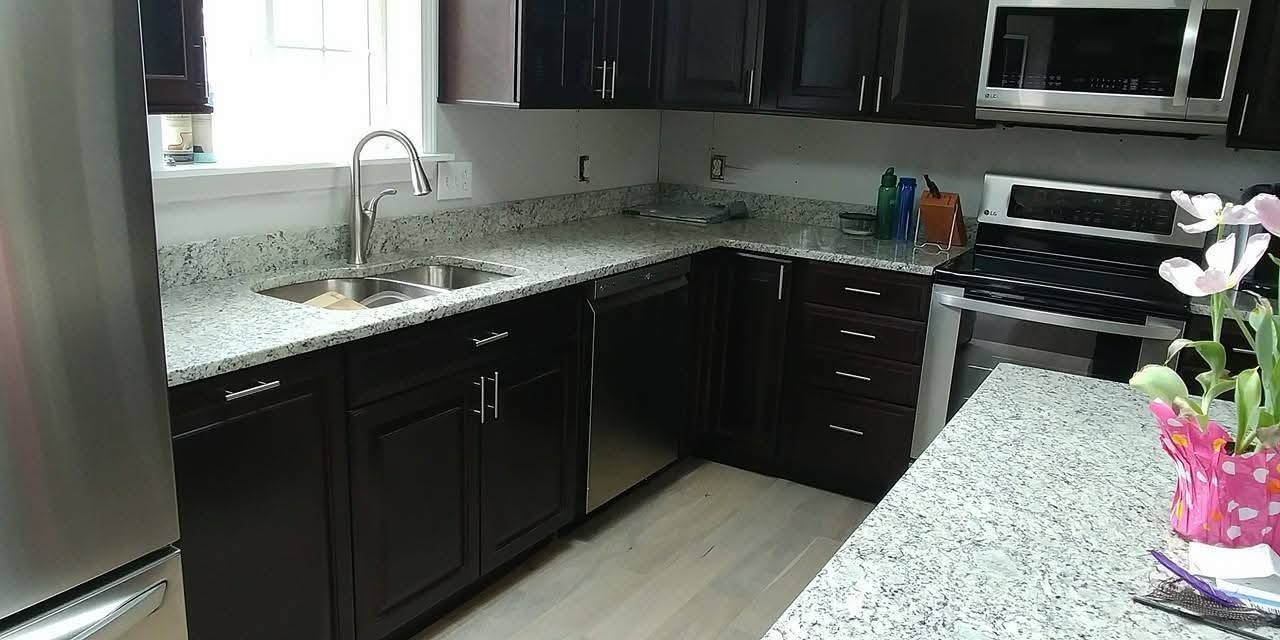 Modern kitchen with dark cabinets, stainless-steel appliances, and a granite countertop with flowers.