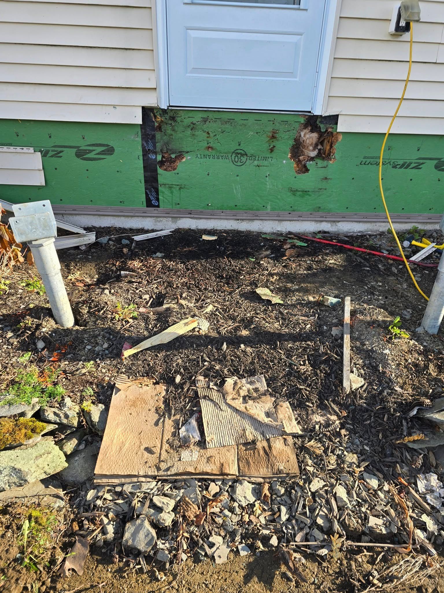 Charred debris and burned ground below a house wall with black scorch marks and a white door above.