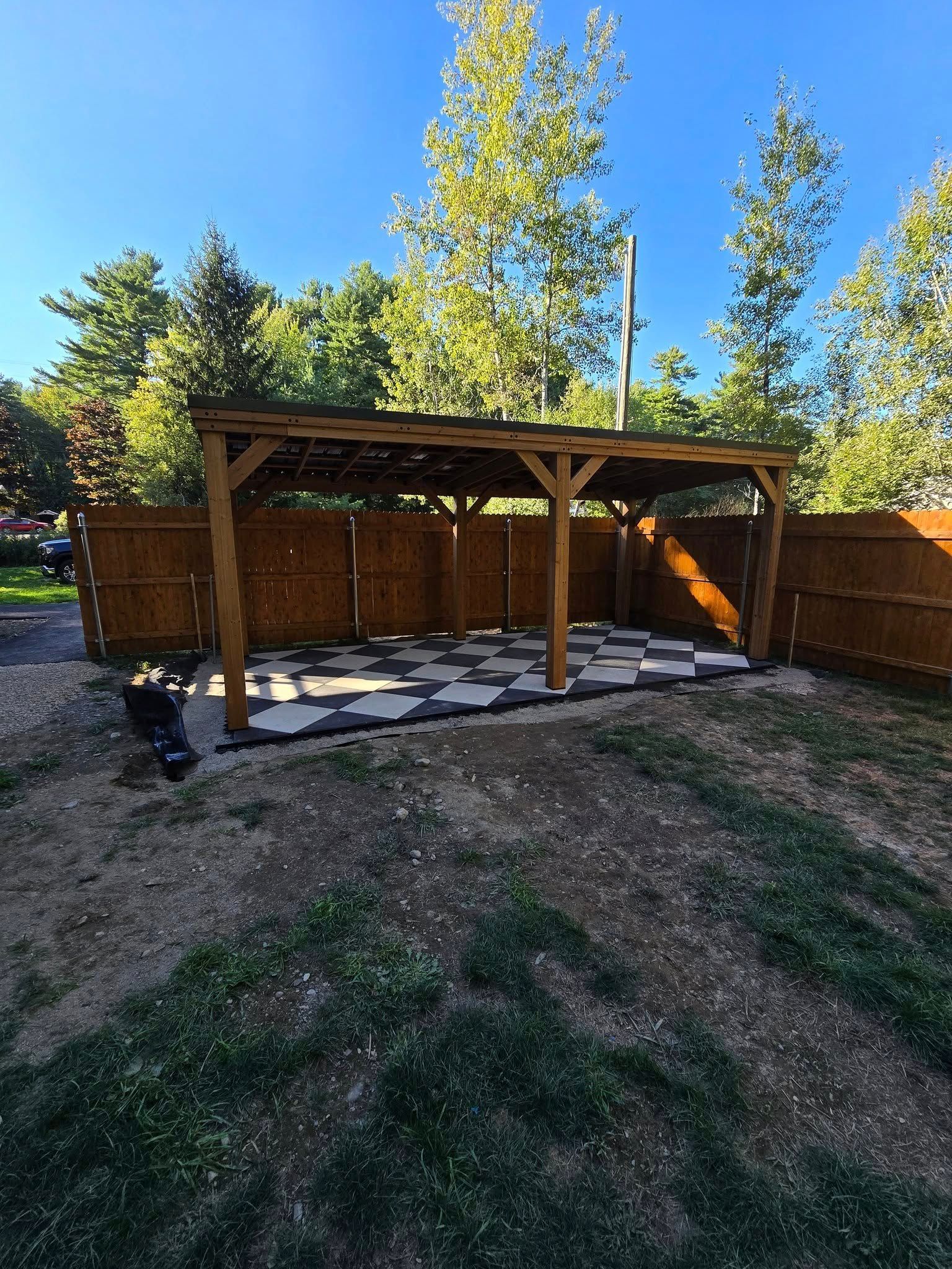 Wooden pergola with a stone patio in a fenced backyard under a clear blue sky