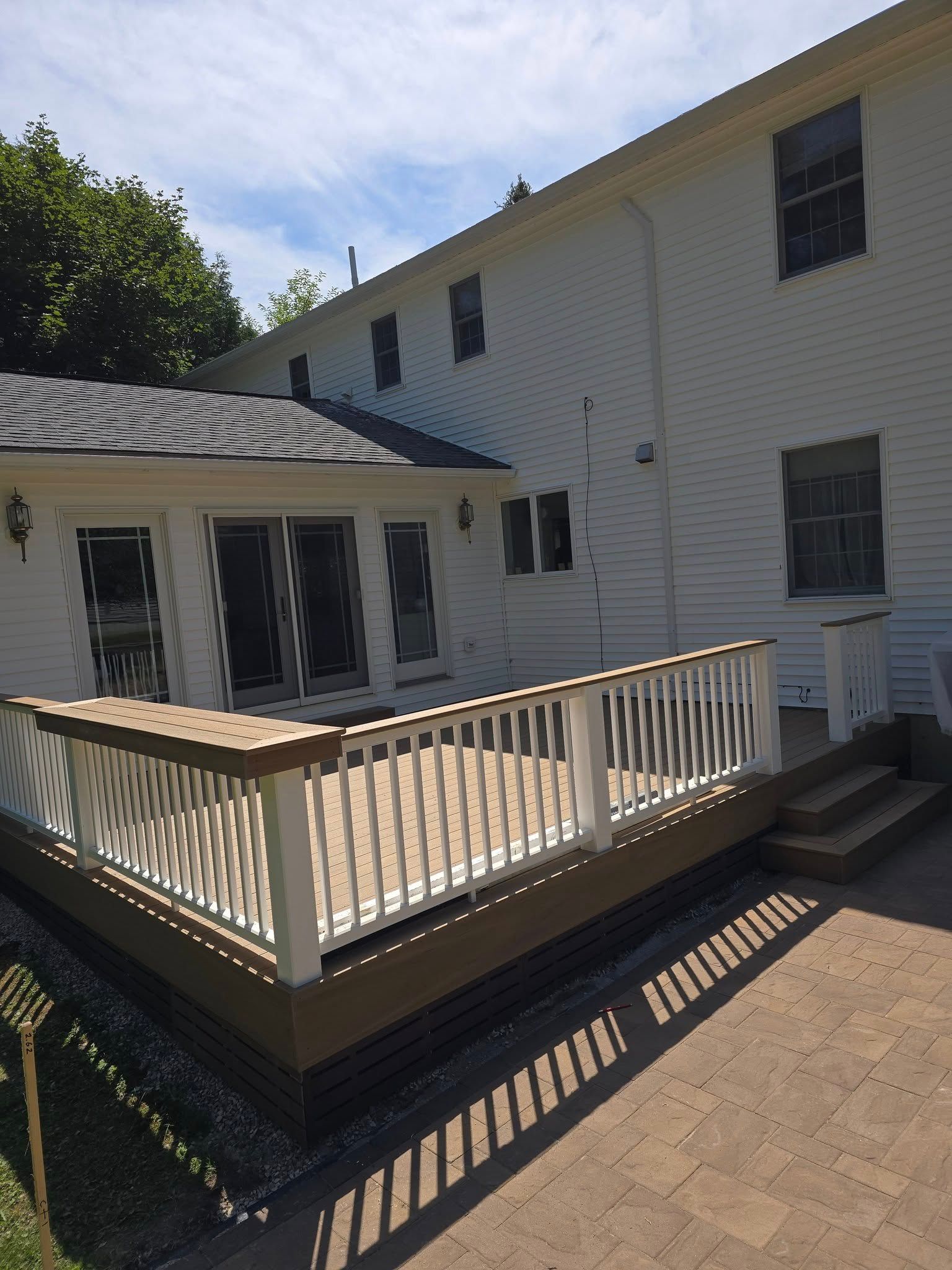 White two-story house with a wooden deck and railing in a sunny backyard