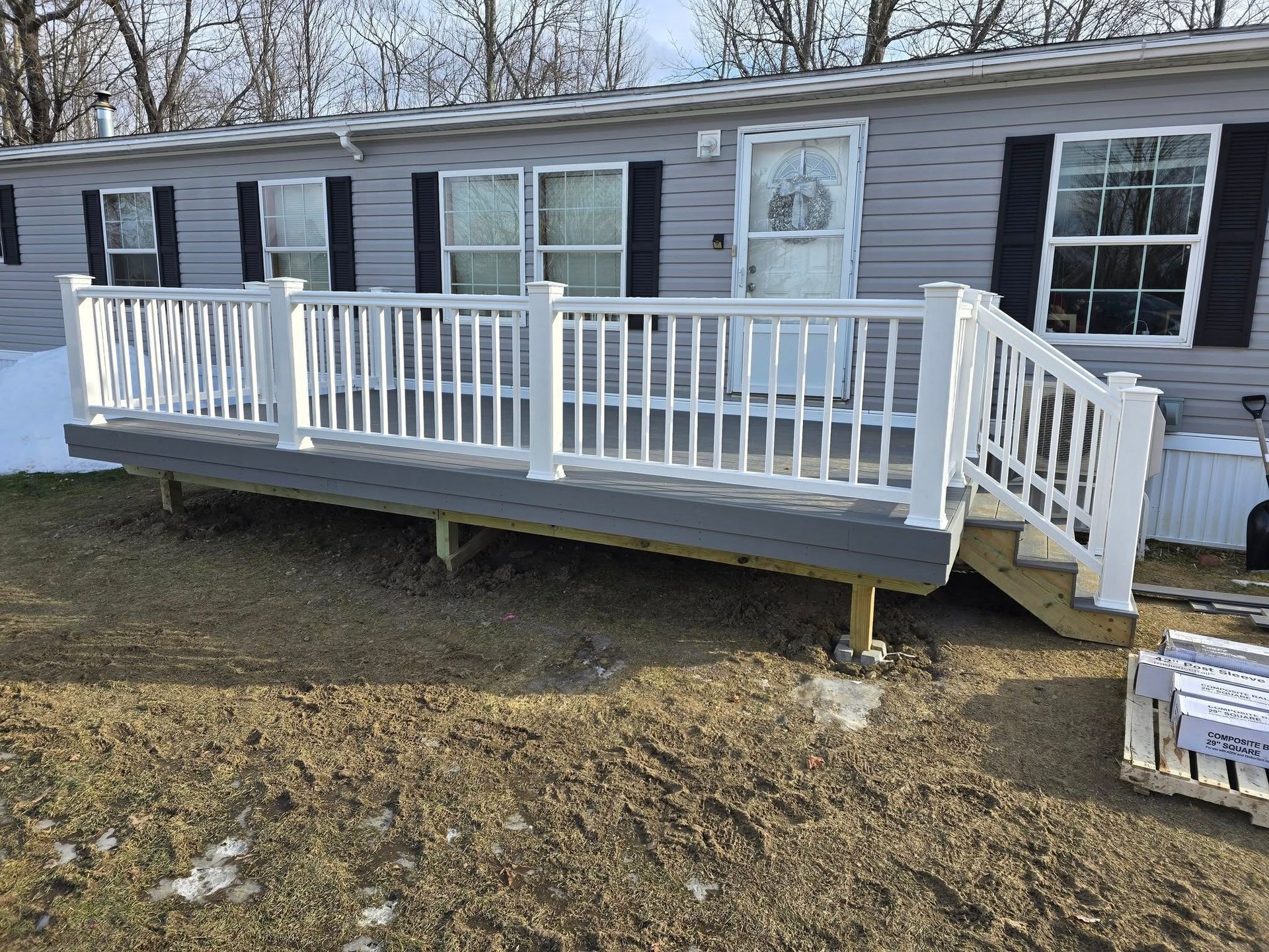 Mobile home with white-railed front porch and steps in a wooded yard