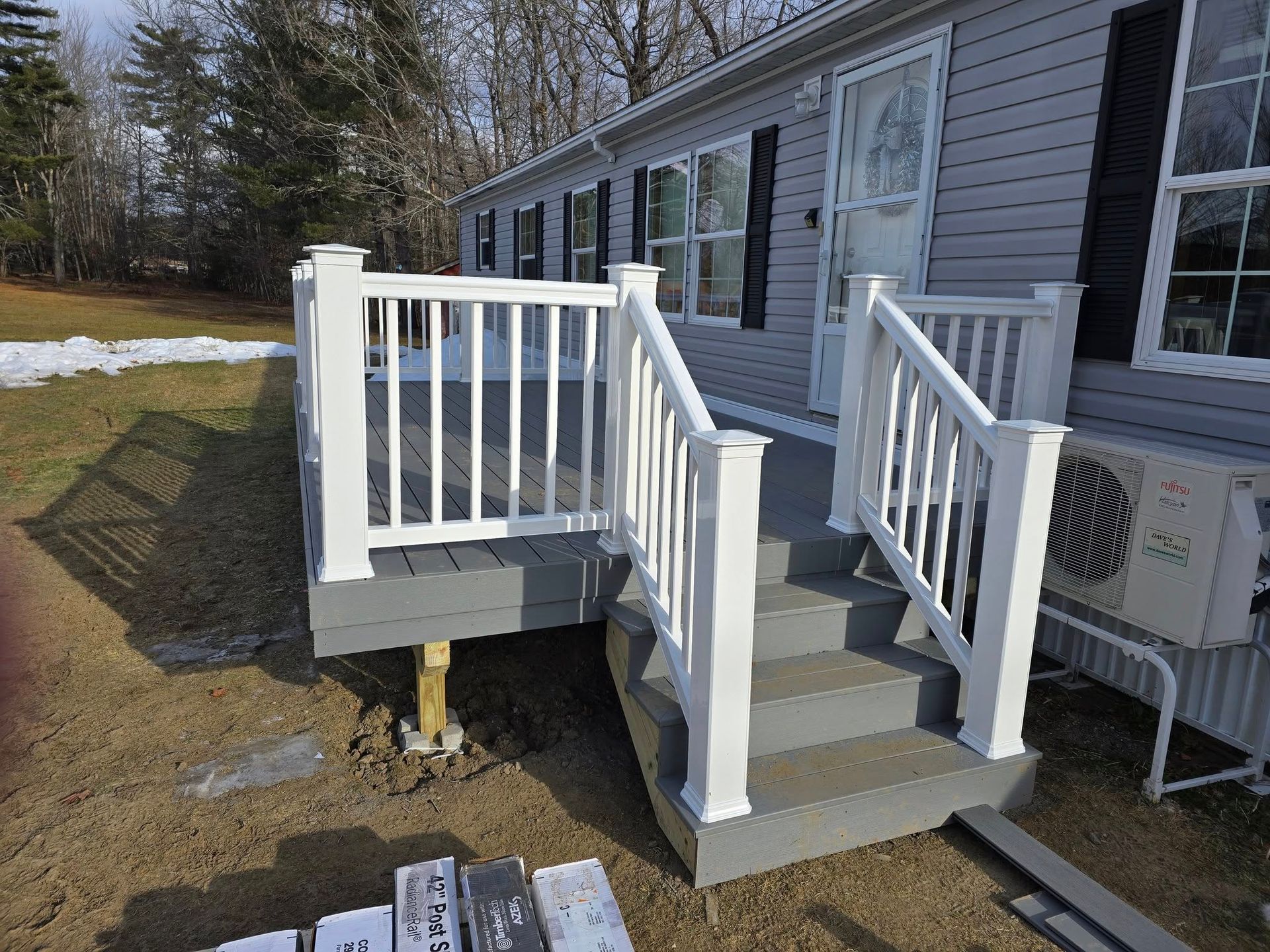 White accessibility ramp and steps leading to a house with a gray exterior and snowy yard.