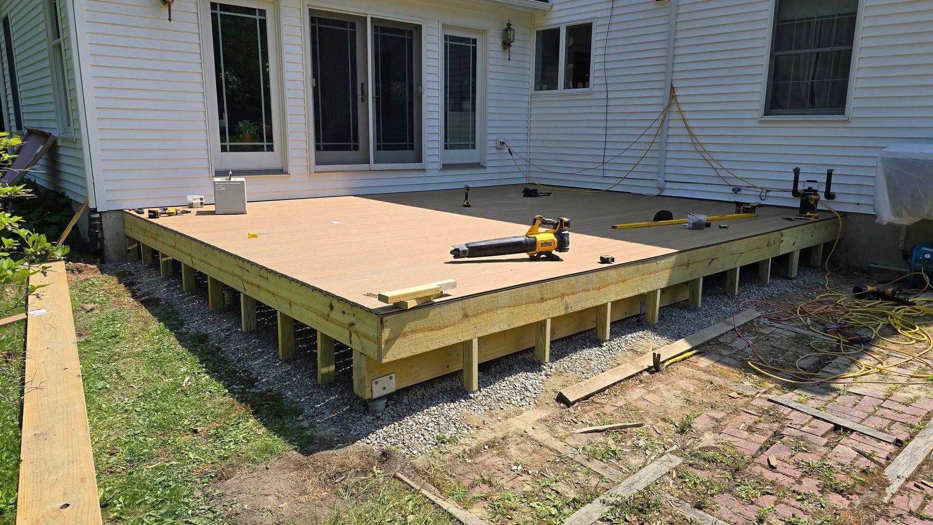 Backyard deck under construction beside a house, with plywood floor and tools on top