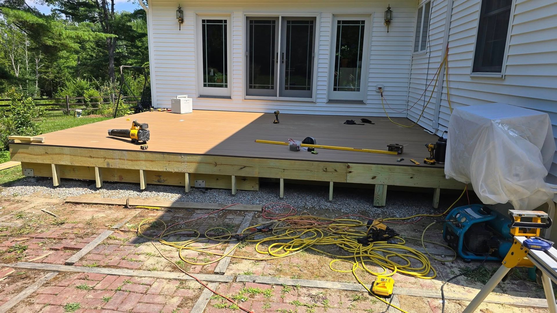 Partially built wooden deck outside a white house, with tools and materials on the patio.