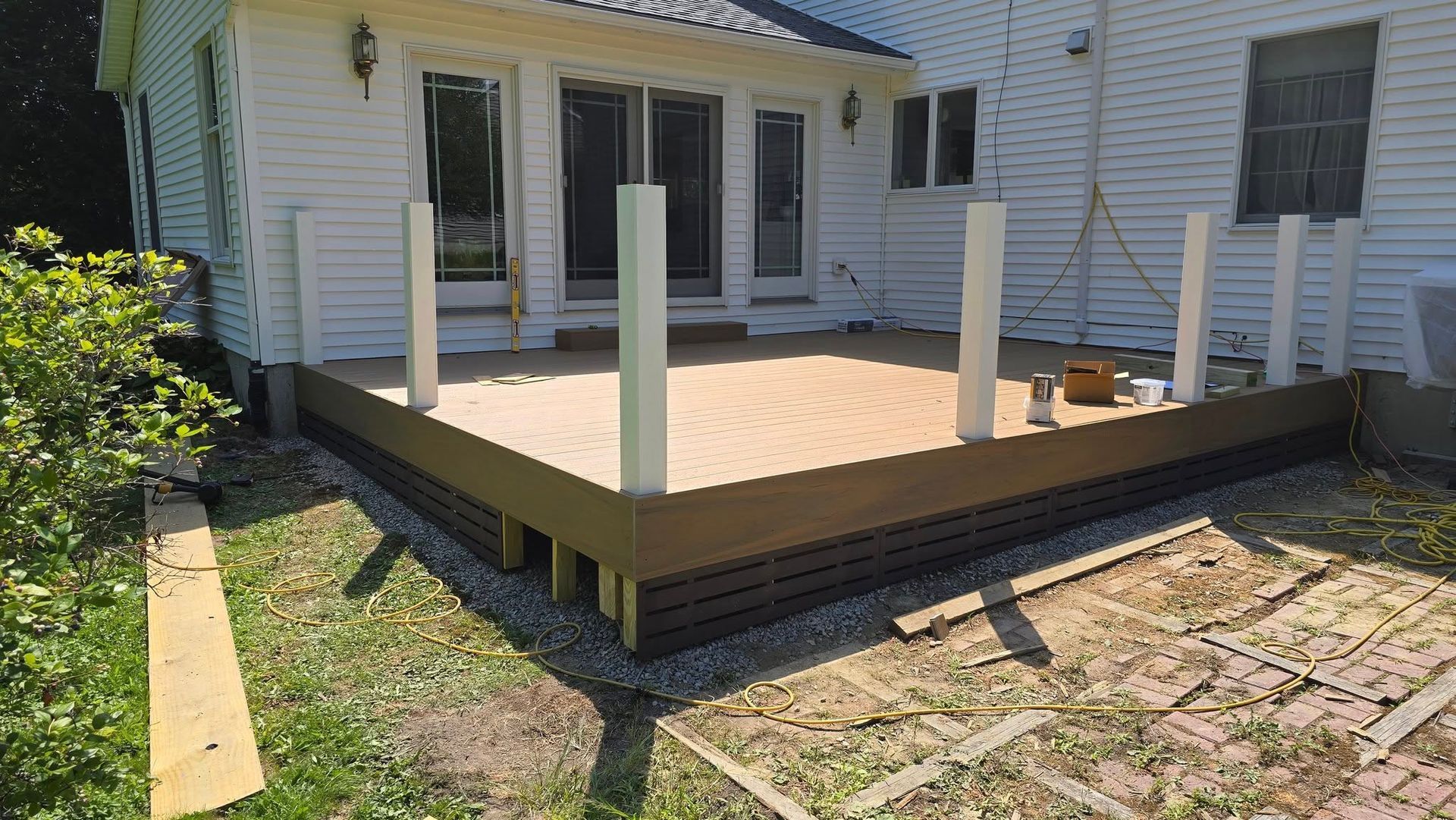 Wooden backyard deck under construction behind a white house, with posts and unfinished railings.