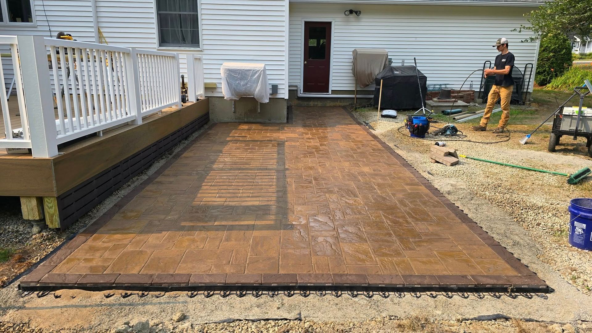 Backyard deck under construction beside a white house, with workers and tools visible.