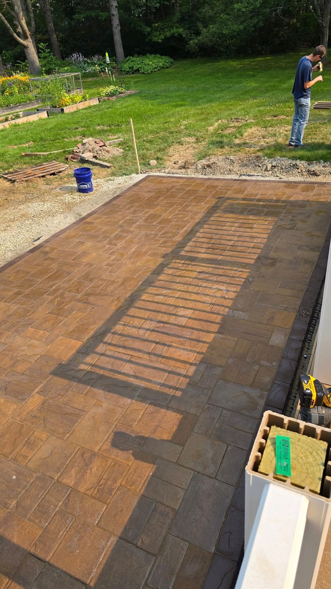 Freshly stained wooden deck under construction in a backyard, with a worker standing at the edge.