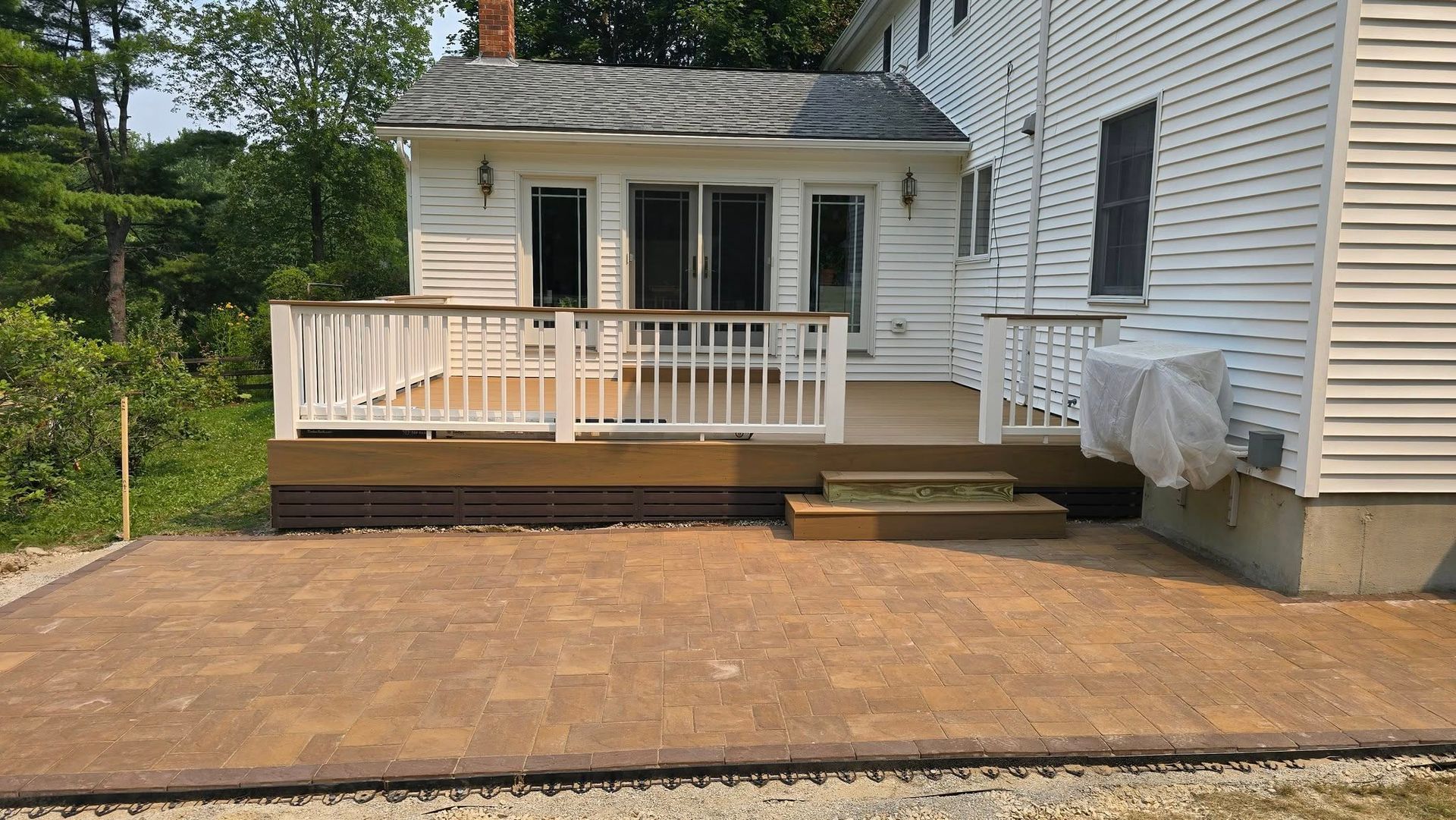 Back deck with white railing and steps beside a house, next to a newly leveled dirt area