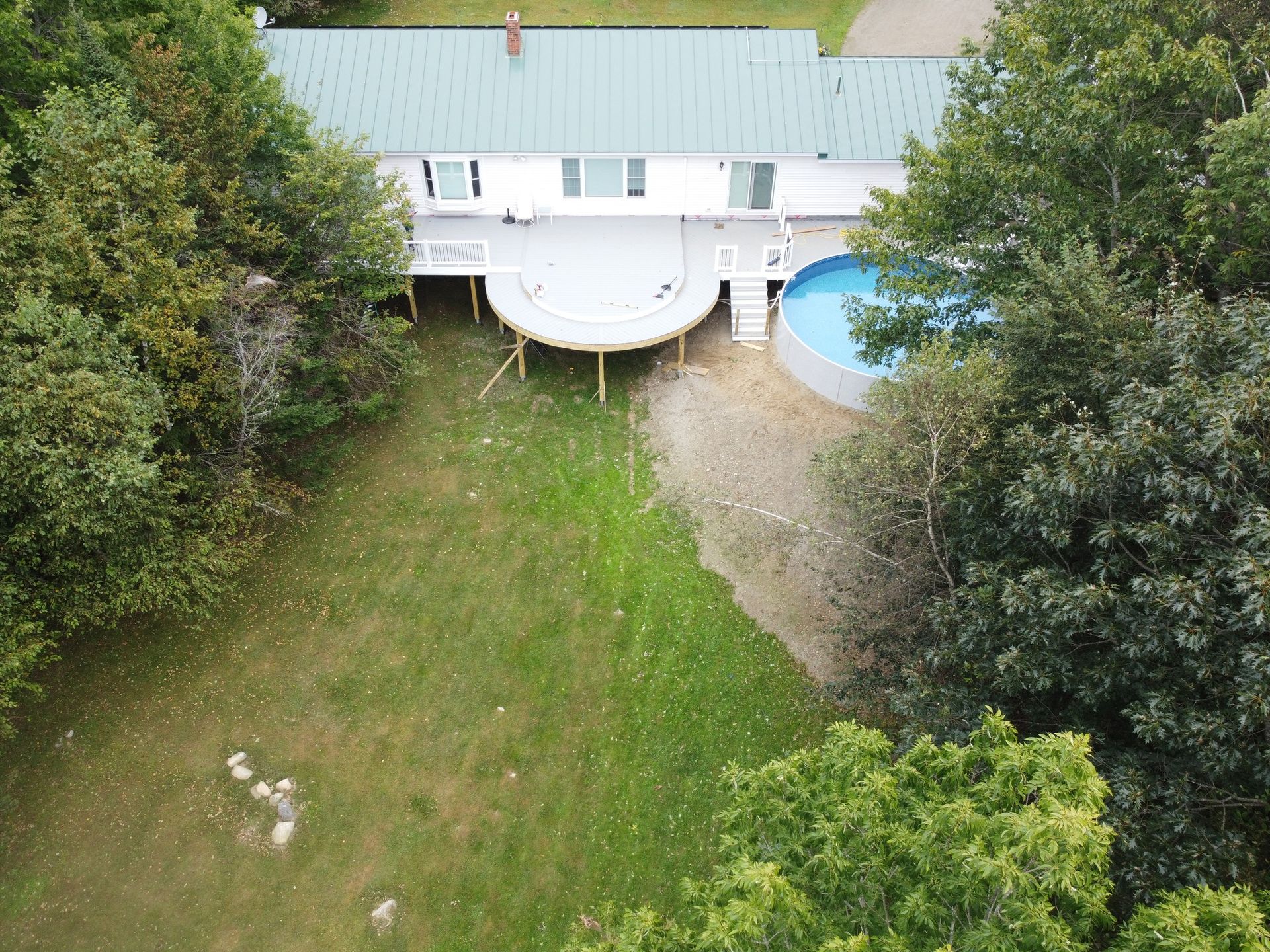 Backyard with green lawn, trees, a white deck, and a blue swimming pool beside the house